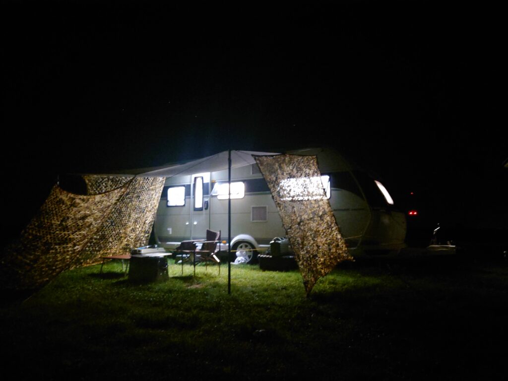 夜のキャンプサイトでライトに照らされたカモフラージュネットとキャンピングトレーラー